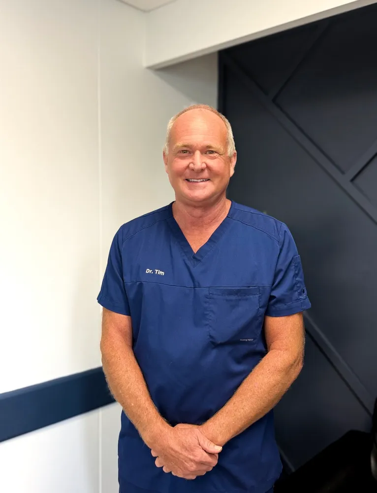 Dr. Timothy D. Andres, DDS, smiling in navy scrubs in the office